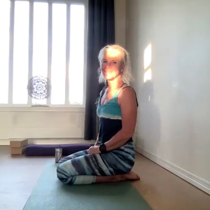 En blond kvinna i medelåldern sitter på golvet i en ljus yogastudio